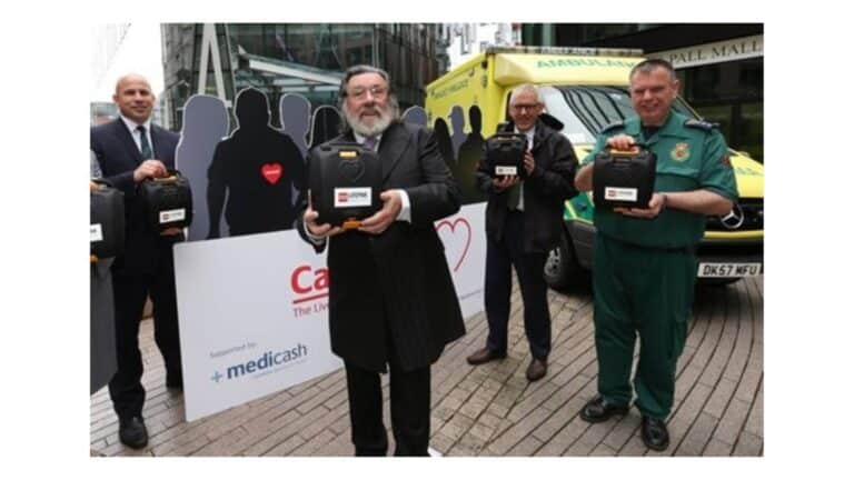 Four males stood in front of an ambulance holding a defibrillator